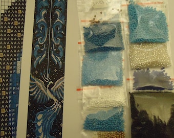 May include: A close-up of a beading kit for a phoenix design. The kit includes a chart, a pattern, and a variety of beads in different colors, including gold, white, blue, and black.