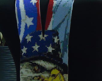 May include: A beaded necklace with a red, white and blue American flag design. The necklace features a beaded image of a bald eagle with a yellow beak and talons. The necklace has a fringe of red, white and blue beads.