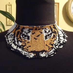 May include: A beaded choker necklace with a tiger face design. The beads are black, white, and gold.