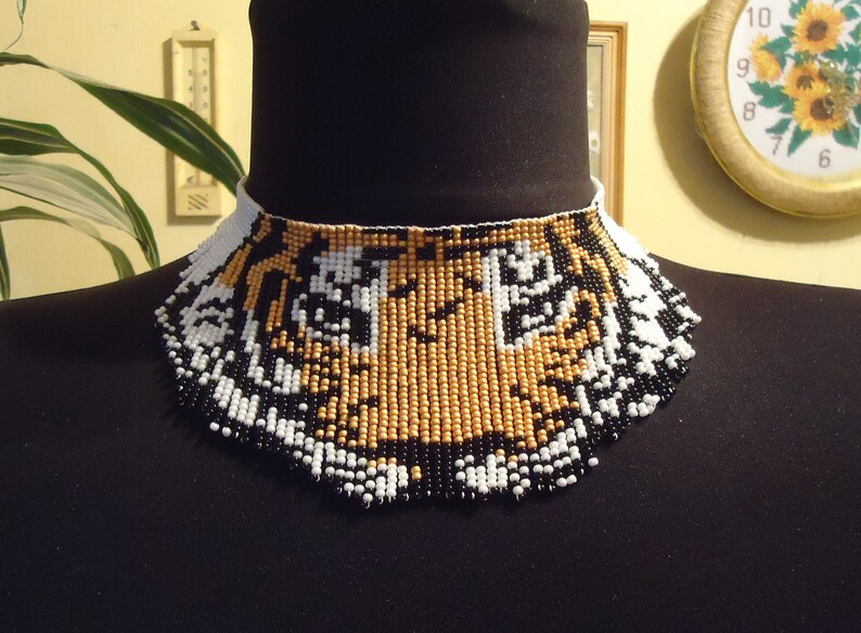 May include: A beaded choker necklace with a tiger face design. The beads are black, white, and gold.