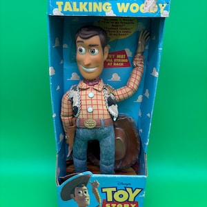 May include: A Woody pull-string talking action figure in its original box. The box is blue with white clouds and the words "PULL-STRING TALKING WOODY". The figure is wearing a cowboy hat, plaid shirt, and blue jeans. The box also says "TRY ME! PULL STRING AT BACK".