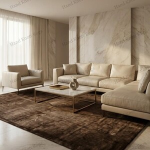 May include: A modern living room featuring a large, brown area rug. The room includes a beige sectional sofa, a matching armchair, and a marble-topped coffee table with a gold frame. The walls are a light beige color.