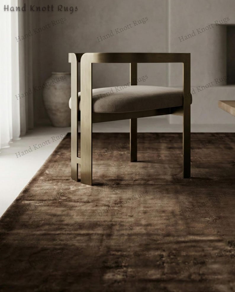 May include: A modern chair with a rectangular metal frame and a cushioned seat sits on a brown rug. The rug has a distressed, textured appearance. The words "Hand Knott Rugs" are printed on the top and sides of the image.