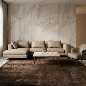 May include: A modern living room featuring a large, brown rug. A beige sectional sofa and a matching armchair are arranged around a marble-topped coffee table with a gold base. The wall is a light marble pattern.