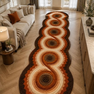 May include: A long, oval-shaped runner rug featuring a repeating pattern of interconnected circular motifs. The rug displays a gradient colour palette of dark brown, terracotta, orange, and cream, with a textured, tufted surface throughout.