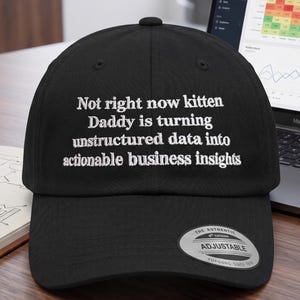 May include: A black baseball cap featuring white embroidered text that reads: Not right now kitten Daddy is turning unstructured data into actionable business insights. The cap includes a silver and black sticker on the brim that says The Authentic Adjustable Yupoong.