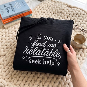 Pu&ograve; includere: Una felpa nera con cappuccio caratterizzata da una scritta ricamata in bianco che recita "if you find me relatable, seek help", circondata da piccoli accenti a forma di stella. Il capo include un cappuccio nero abbinato con coulisse.