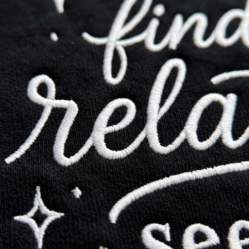 Pu&ograve; includere: Una superficie in tessuto nero con testo ricamato in bianco in corsivo che recita find, rela e see. Il ricamo include piccoli accenti a forma di stella a quattro punte sparsi tra le righe di testo, creando un aspetto strutturato e in rilievo.