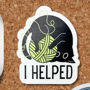 May include: A die-cut sticker featuring a black cat playfully tangled with a ball of yarn. The cat's silhouette is above a white rectangle with the words "I HELPED" in bold, black letters. The yarn is a light green color.