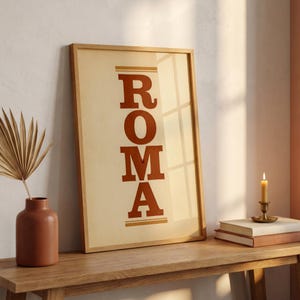 May include: A rectangular framed print featuring the word ROMA in bold, dark orange capital letters stacked vertically on a light beige background. The print is enclosed in a light-toned wooden frame, displaying a clean and simple design.