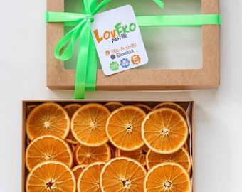 Può includere: Una confezione regalo in cartone con una finestra trasparente, legata con un nastro verde e un'etichetta con la scritta "LoveEko pastille". La scatola contiene fette di arancia essiccate. Lo schema cromatico è naturale e terroso.