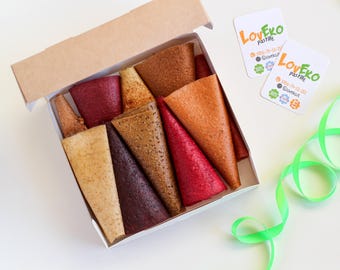 Op de afbeelding: Een witte kartonnen doos gevuld met diverse rollen fruitleer in tinten rood, oranje, bruin en beige. Twee witte vierkante kaarten met de tekst "LovEko pastille" en contactgegevens liggen naast de doos met een groen lint.