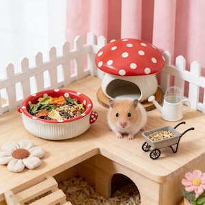 Puede incluir: Un hábitat para hámsteres con una casa con forma de hongo rojo y blanco, un cuenco de cerámica con comida y una carretilla en miniatura. El hábitat es de madera e incluye un pequeño hámster.
