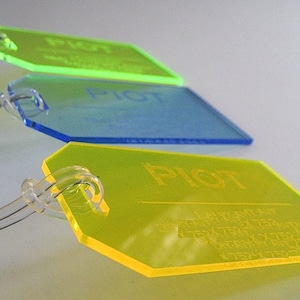 May include: Three luggage tags with the word "PIOT" printed on them. The tags are made of clear plastic and are in the colors green, blue, and yellow.