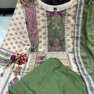 May include: A beige and green printed tunic and matching green pants. The tunic features a detailed floral and geometric pattern with accents of purple and gold. The outfit includes a matching green scarf. The text "SHREEVIL" is visible.
