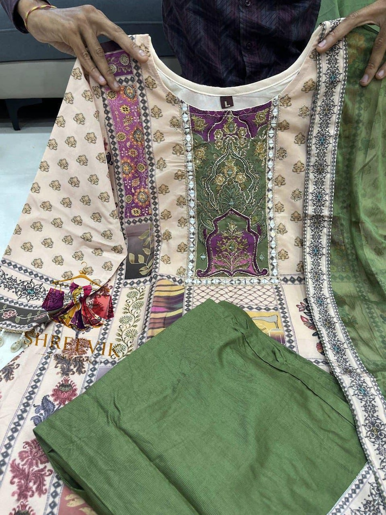 May include: A beige and green printed tunic and matching green pants. The tunic features a detailed floral and geometric pattern with accents of purple and gold. The outfit includes a matching green scarf. The text "SHREEVIL" is visible.
