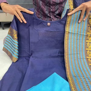 May include: A navy blue kurta set with a matching dupatta. The kurta features short sleeves with gold and turquoise patterned cuffs. A turquoise fabric is visible at the bottom. The set is held up by a person.