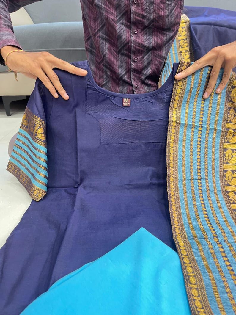 May include: A navy blue kurta set with a matching dupatta. The kurta features short sleeves with gold and turquoise patterned cuffs. A turquoise fabric is visible at the bottom. The set is held up by a person.