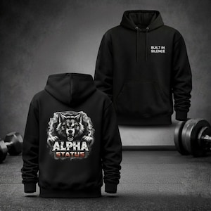 Peut inclure: Sweat à capuche noir avec un motif de loup et le texte "ALPHA STATUS" au dos. Le devant du sweat à capuche porte l'inscription "BUILT IN SILENCE". Le design est en nuances de gris et de blanc, sur fond noir. Le sweat à capuche a une capuche et une poche avant.