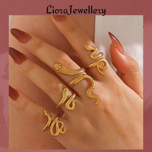 Puede incluir: Anillos de serpiente dorados en varios diseños. Los anillos se envuelven alrededor de los dedos, con detalles de cabeza y cuerpo de serpiente. Las joyas se muestran en una mano con uñas largas y pulidas.