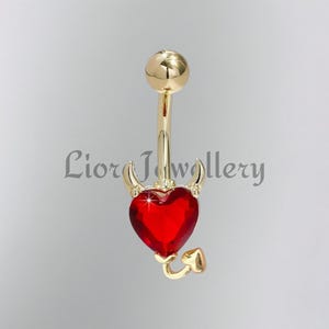 Può includere: Un piercing all'ombelico color oro con un gioiello rosso a forma di cuore. Il cuore è adornato da piccole corna e una coda, creando un design diabolico. Il testo "Lior Jewellery" è visibile.