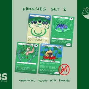 May include: A set of four rectangular trading cards titled FROGSIES SET 2, featuring illustrations of frogs labelled Omnibian, Spore Frog, Polliwallop, and Grolnok, the Omnivore. The cards include game text, power and toughness stats, and a red AI symbol.