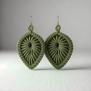 Könnte beinhalten: Ein Paar olivgrüne, blattförmige Ohrringe. Jeder Ohrring hat ein gewebtes Design mit einem zentralen Spiralmuster und einem geflochtenen Rand. Sie hängen an goldfarbenen Ohrhaken.