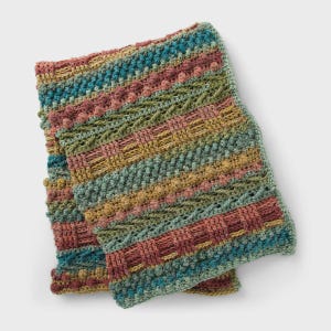 Può includere: Una sciarpa multicolore all'uncinetto a mano con un design strutturato. La sciarpa presenta strisce orizzontali nei toni del verde acqua, rosa, verde e oro. Il motivo include pompon, sezioni intrecciate e dettagli traforati, creando un accessorio accogliente e visivamente accattivante.