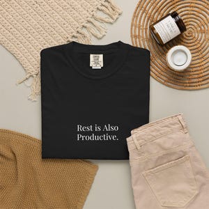 Könnte beinhalten: Ein schwarzes kurzärmeliges T-Shirt mit dem weißen Text "Rest is Also Productive." auf der Vorderseite. Das T-Shirt hat einen Rundhalsausschnitt und ein Comfort Colors Markenetikett am inneren Kragen, das die Größe Large angibt.