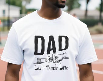 May include: A white short-sleeved t-shirt featuring the black text DAD above a graphic of an adult fist bumping a child's hand, with the text Lead-Teach-Love printed in black below the graphic on the front of the garment.