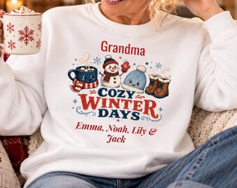 May include: A white crewneck sweatshirt featuring a graphic with the text Grandma, Cozy Winter Days, and the names Emma, Noah, Lily & Jack. The design includes a snowman, a blue knit hat, brown boots, and a mug with a red and white scarf.