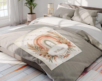 May include: A rectangular throw blanket featuring a printed design of a muted rainbow, dried pampas grass, and floral elements. A central scalloped label contains the name William in a dark script font. The blanket has a cream background.