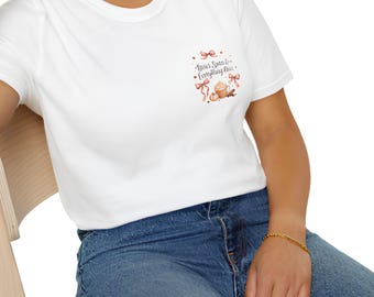 May include: A white short-sleeved t-shirt featuring a small graphic on the left chest. The design includes pink bows, a mug of coffee, and the text "Twas Spiced to Everything Nice" in a dark script font, paired with blue denim jeans.