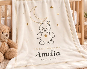 May include: A cream-colored fleece blanket featuring a gold crescent moon, stars, and a central teddy bear graphic. The text reads "SWEET DREAMS", "Amelia", and "EST. 2026" in black and gold lettering, framed by a thin gold rectangular border.