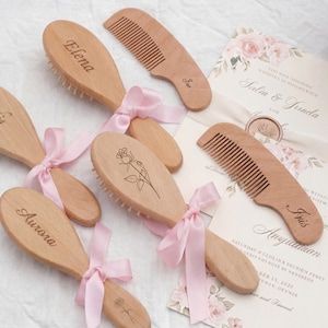 Puede incluir: Cepillos y peines de madera con nombres personalizados y diseños florales. Cada cepillo está atado con una cinta rosa. También se ven invitaciones de boda con detalles florales.