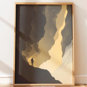 May include: A framed vertical wall art print featuring a silhouette of a person standing on a dark rocky ledge, holding a bright light source. The scene depicts a deep, cavernous landscape with layered shades of charcoal, grey, and soft yellow.