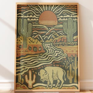 May include: A framed wall art print featuring a desert landscape illustration with a large orange sun, saguaro cacti, a winding river, and a bison in the foreground. The color palette consists of muted olive green, burnt orange, and cream tones.
