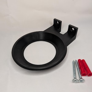 May include: A black wall mount, 3D-printed with a circular aperture and mounting brackets. Includes two screws and two red wall plugs for installation. Designed to hold a round object.