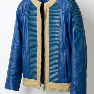 May include: A blue leather jacket featuring a stand-up collar, a central zipper, and textured beige fabric panels along the front and hem. The shoulders and chest panels have horizontal ribbed detailing, and the number 76 is printed on the inner collar.