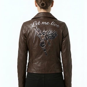 May include: A brown leather jacket featuring a back graphic of a winged figure holding a sword, with the text Let me live printed above the illustration. The jacket has a collared neckline, long sleeves with zippered cuffs, and a fitted waistline.