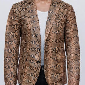 May include: A blazer featuring a brown and black snakeskin pattern with a notched lapel, two front flap pockets, and a two-button closure. The garment is worn over a plain white undershirt and paired with black trousers.
