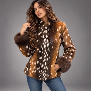 May include: A long-sleeved jacket featuring a brown and white spotted pattern reminiscent of a fawn's coat. The garment includes dark brown fur cuffs at the wrists and a high collar, paired with blue denim jeans. The texture appears soft and plush.
