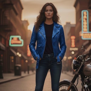 Peut inclure: Veste en cuir bleu à motif peau de serpent, de style motard classique. La veste présente un col cranté, une fermeture éclair asymétrique et une ceinture à la taille. Le modèle porte un t-shirt noir et un jean bleu. Une moto est garée en arrière-plan.