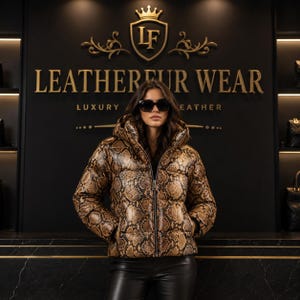 Könnte beinhalten: Eine Kapuzen-Daunenjacke mit braun-schwarzem Schlangenledermuster und Frontreißverschluss. Im Hintergrund befindet sich eine schwarze Wand mit goldener Aufschrift LEATHERFUR WEAR LUXURY LEATHER und einem Kronenlogo über dem Text.