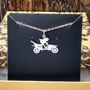 May include: A silver necklace with a pendant of a couple riding in a vintage car. The necklace is displayed in a brown box with a black velvet insert.