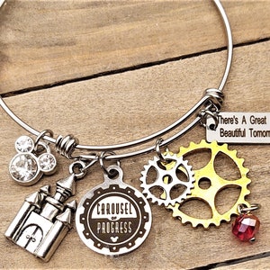 May include: A silver bangle bracelet with charms including a castle, a Mickey Mouse head, gears, and a tag that reads "There's A Great BIG Beautiful Tomorrow".