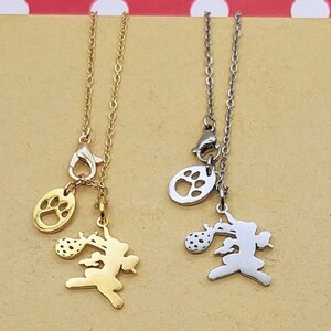 May include: Two necklaces with a paw print charm and a charm of a dog running with a ball in its mouth. One necklace is gold and the other is silver.