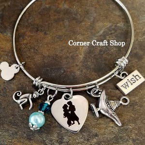 May include: A silver charm bracelet with a heart charm featuring a silhouette of a couple, a monkey charm, a genie lamp charm, a blue crystal charm, a pearl charm, and a charm with the word "wish" on it.