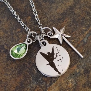 May include: A silver necklace with a charm featuring a silhouette of Tinkerbell, a green crystal teardrop, and a star-shaped wand.