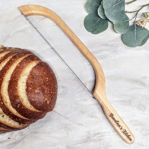 May include: A wooden bread knife with a curved blade and a wooden handle. The handle is engraved with the text "Grandma's Kitchen".
